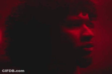 A Close Up Of A Man 'S Face In A Dark Room With A Red Light Behind Him GIF
