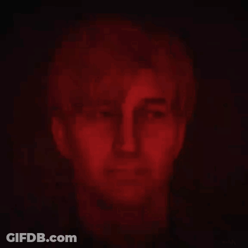 A Close Up Of A Man 'S Face In A Dark Room With Red Lights Behind Him . GIF