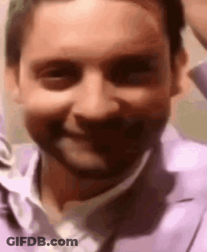 A Close Up Of A Man 'S Face In A Purple Shirt And Tie Smiling . GIF