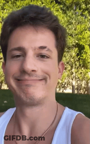 A Close Up Of A Man 'S Face Wearing A White Tank Top And A Gold Chain . GIF