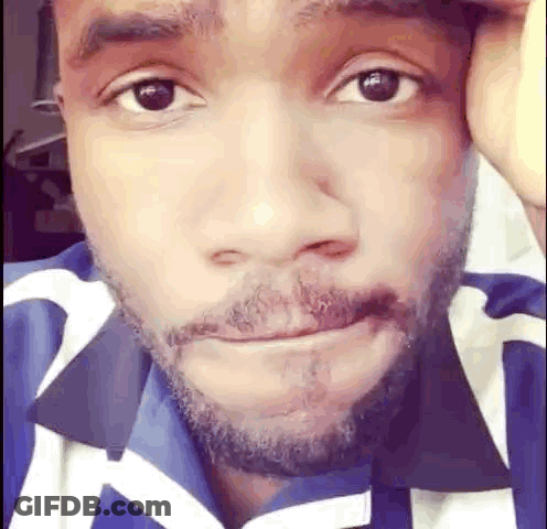 A Close Up Of A Man 'S Face With A Beard And A Blue And White Shirt . GIF