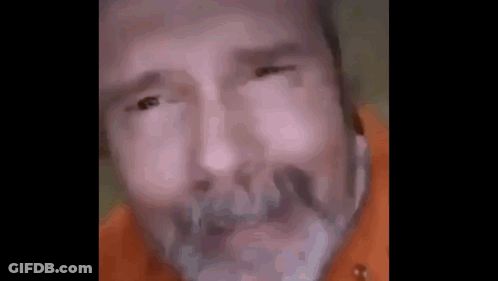 A Close Up Of A Man 'S Face With A Beard And A Orange Shirt . GIF