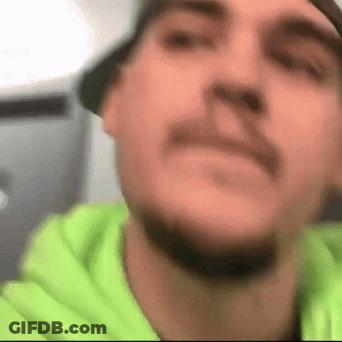 A Close Up Of A Man 'S Face With A Beard Wearing A Green Hoodie GIF