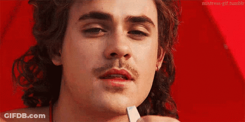 A Close Up Of A Man 'S Face With A Mustache Holding A Piece Of Paper In His Hand . GIF