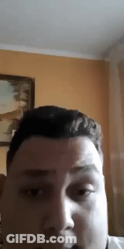 A Close Up Of A Man 'S Face With A Painting On The Wall Behind Him . GIF