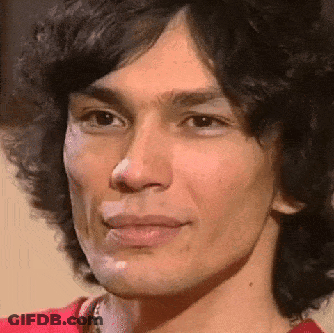 A Close Up Of A Man 'S Face With A Red Shirt On And A Necklace Around His Neck . GIF