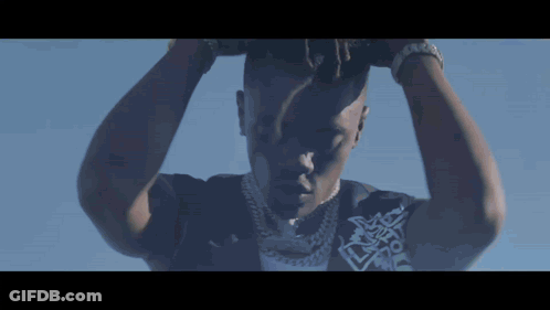 A Close Up Of A Man 'S Face With His Hands On His Head Against A Blue Sky GIF