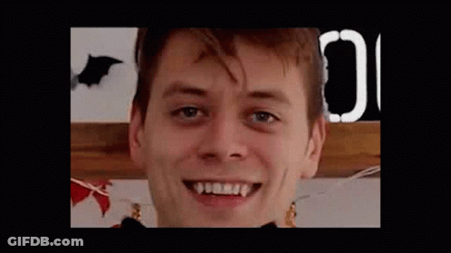 A Close Up Of A Man 'S Face With Vampire Teeth And A Bat In The Background . GIF