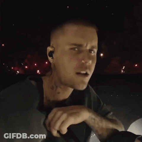 A Close Up Of A Man Singing Into A Microphone With Fireworks In The Background GIF