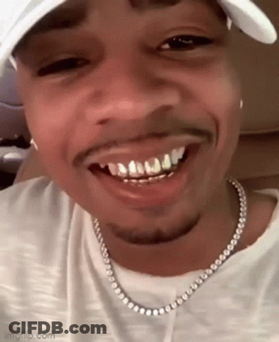 A Close Up Of A Man Wearing A Hat And A Necklace With His Teeth Visible . GIF