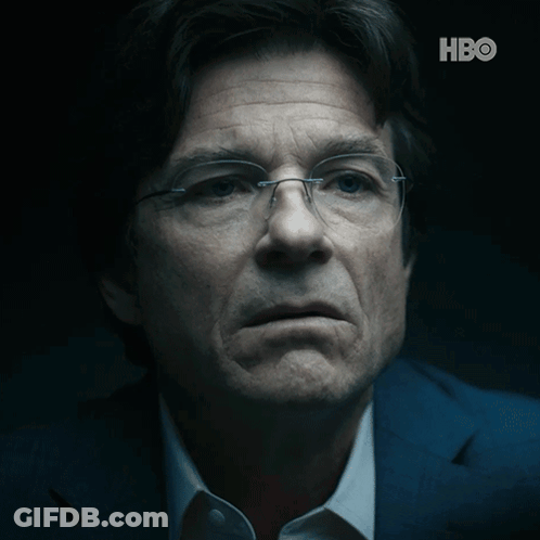 A Close Up Of A Man Wearing Glasses And A Suit With The Hbo Logo Behind Him GIF