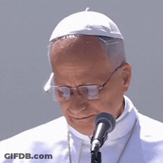 A Close Up Of A Man Wearing Glasses And A White Hat Speaking Into A Microphone GIF