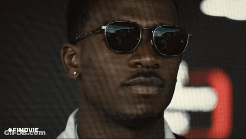 A Close Up Of A Man Wearing Sunglasses With #Fimovie Written Below Him GIF