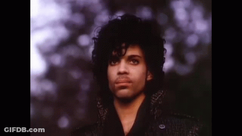 A Close Up Of A Man With Curly Hair Wearing A Black Coat And Looking At The Camera . GIF