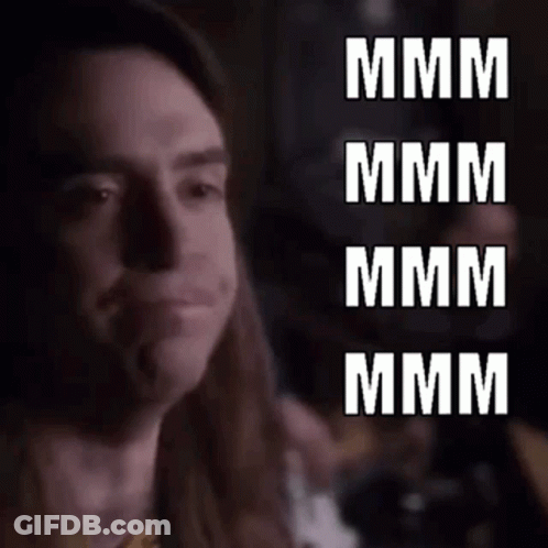 A Close Up Of A Man With Long Hair Making A Funny Face With The Words `` Mmmm '' Written In White Letters . GIF