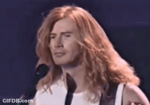 A Close Up Of A Man With Long Hair Singing Into A Microphone GIF