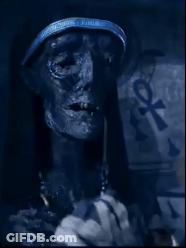 A Close Up Of A Mummy With An Ankh Symbol On The Wall Behind Him GIF