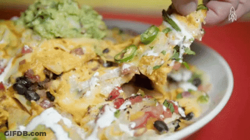 A Close Up Of A Person Eating Nachos With Guacamole On Top GIF
