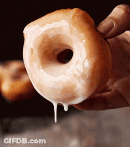A Close Up Of A Person Holding A Glazed Doughnut GIF
