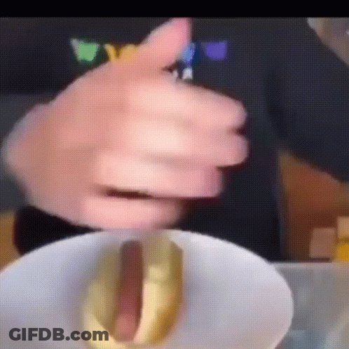 A Close Up Of A Person Holding A Hot Dog With Mustard On It GIF