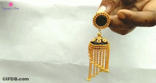 A Close Up Of A Person Holding A Pair Of Gold Earrings With A Black Circle In The Middle GIF