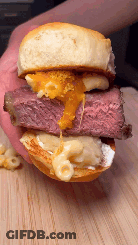 A Close Up Of A Person Holding A Sandwich With Meat And Cheese On A Bun GIF
