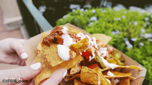 A Close Up Of A Person Holding A Tray Of Nachos With The Word Delish On The Bottom GIF