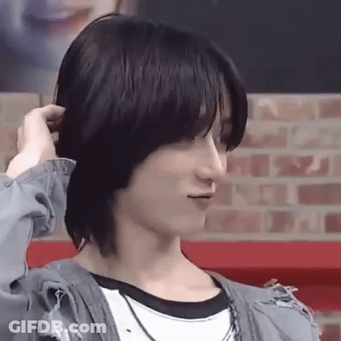 A Close Up Of A Person Holding Their Hair While Standing In Front Of A Brick Wall . GIF