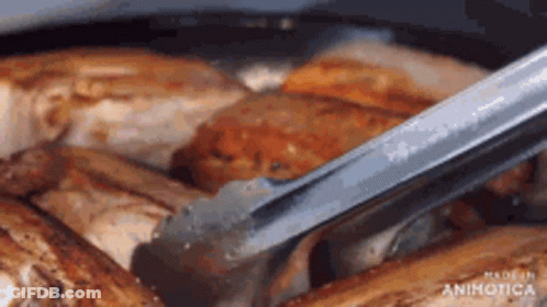 A Close Up Of A Person Holding Tongs Over A Pan Of Meat . GIF