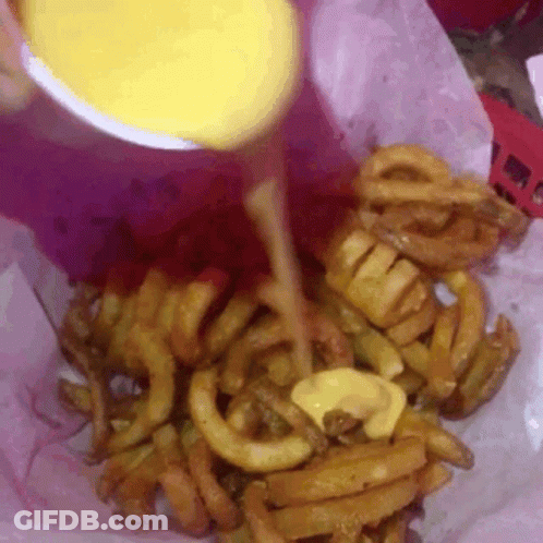 A Close Up Of A Person Pouring Cheese On Curly Fries GIF