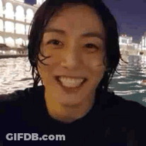 A Close Up Of A Person 'S Face Smiling In Front Of A Body Of Water At Night . GIF