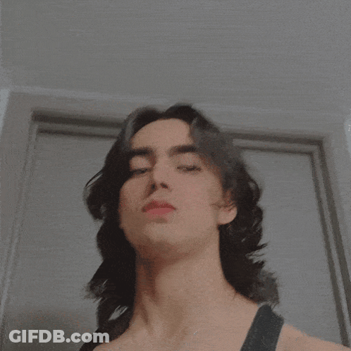 A Close Up Of A Person 'S Face With A Necklace That Says ' I ' On It GIF