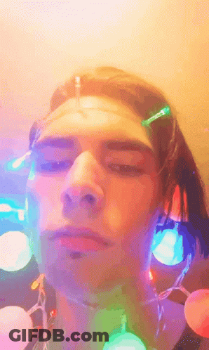 A Close Up Of A Person 'S Face With Christmas Lights Around His Neck GIF