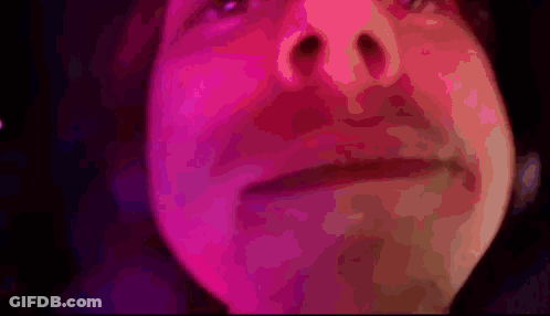 A Close Up Of A Person 'S Face With Pink And Purple Lights Behind Them GIF
