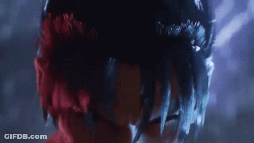 A Close Up Of A Person 'S Face With Red And Black Hair And A Purple Background . GIF