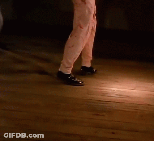 A Close Up Of A Person 'S Feet Wearing Black Shoes Walking On A Wooden Floor . GIF