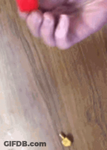A Close Up Of A Person 'S Hand Holding A Red Object On A Wooden Table . GIF