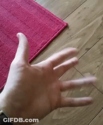 A Close Up Of A Person 'S Hand Reaching Out Towards A Pink Rug On A Wooden Floor . GIF