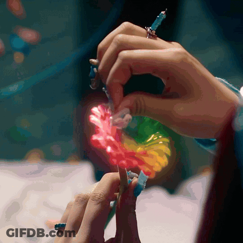 A Close Up Of A Person 'S Hands Holding A Rainbow Colored Flower GIF