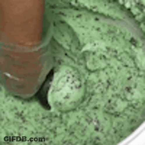 A Close Up Of A Person Scooping Mint Chocolate Chip Ice Cream Into A Bowl . GIF