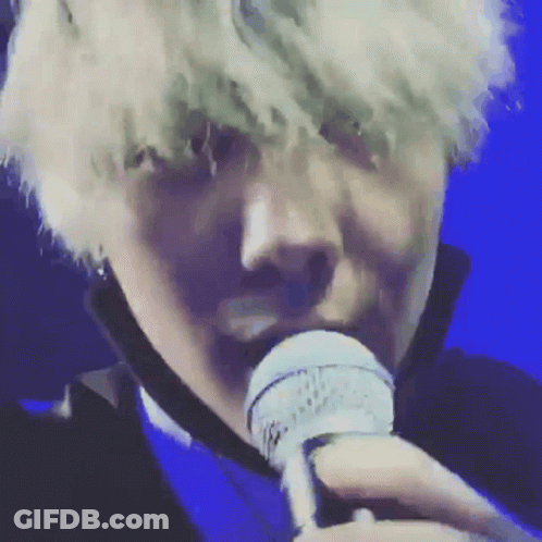A Close Up Of A Person Singing Into A Microphone With A Blue Background GIF