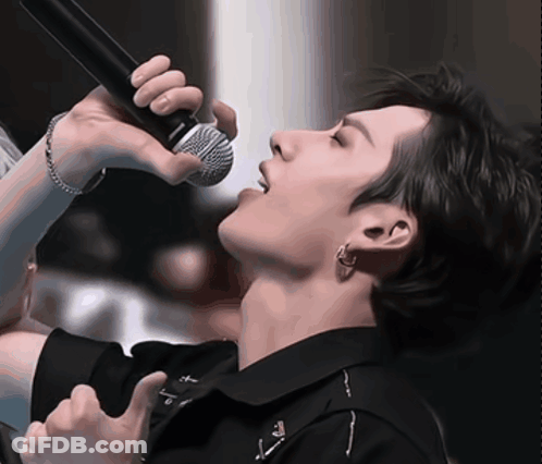A Close Up Of A Person Singing Into A Microphone With The Letter T On His Shirt GIF
