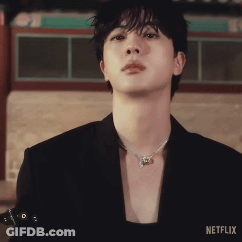 A Close Up Of A Person Wearing A Black Jacket And A Necklace With Netflix Written On The Bottom GIF