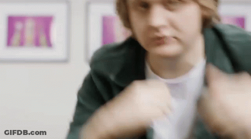 A Close Up Of A Person Wearing A Green Jacket And A White T-Shirt In A Room . GIF