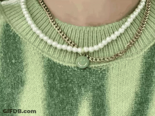A Close Up Of A Person Wearing A Green Sweater And A Necklace With A Smiley Face Pendant . GIF