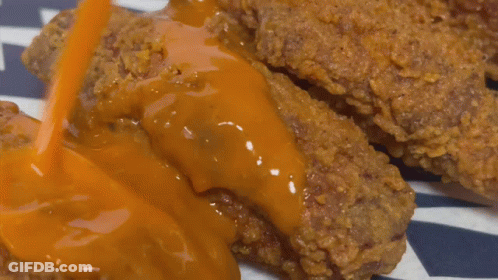 A Close Up Of A Piece Of Fried Chicken Covered In Sauce GIF