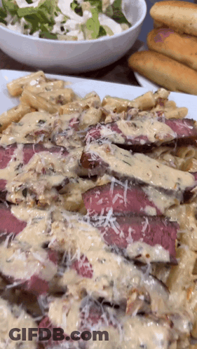 A Close Up Of A Plate Of Food With A Bowl Of Salad In The Background GIF