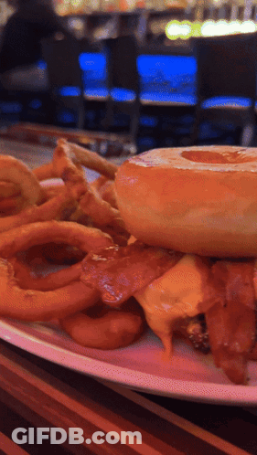 A Close Up Of A Plate Of Food With A Hamburger And Onion Rings GIF