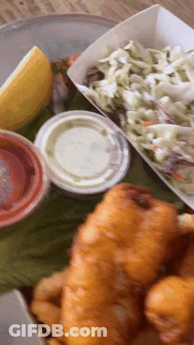 A Close Up Of A Plate Of Food With Coleslaw And A Slice Of Lemon GIF