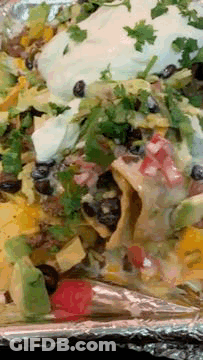 A Close Up Of A Plate Of Nachos With Avocado And Sour Cream On Aluminum Foil GIF